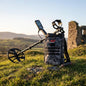 Metal detector and backpack on grass with ruins in the background