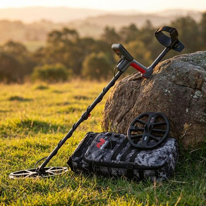Metal detector and accessories in grassy field leaning against a rock