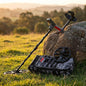 Metal detector and accessories in grassy field leaning against a rock