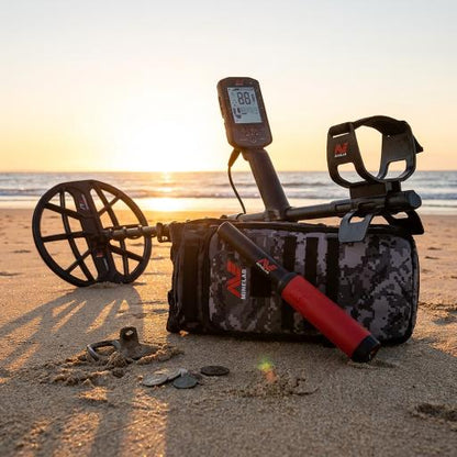 Metal detector and accessories on a sandy beach with coins nearby during sunset.