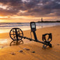 Metal detector on a beach with a lighthouse in the distance during sunset.